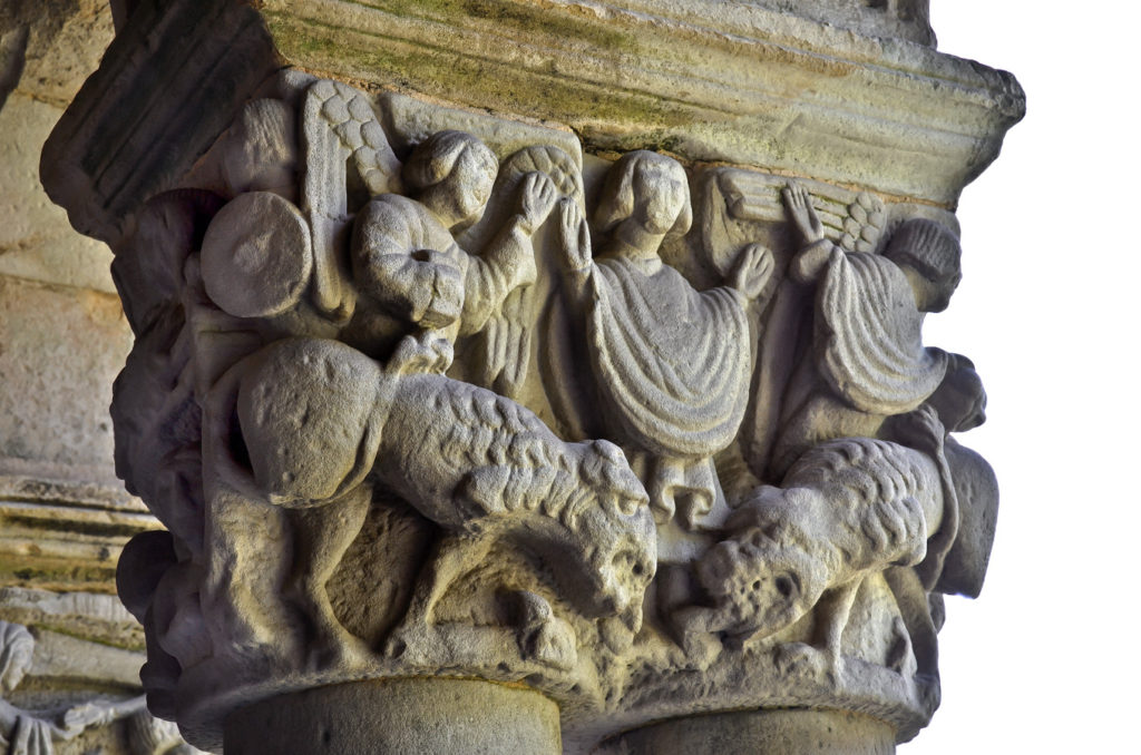 Capitel del claustro de la Real Colegiata de Santa Juliana en Santillana del Mar Cantabria donde se representa a Daniel en el foso de los leones ambas fieras sumisas a sus pies gracias a la ayuda divina explicitada por los dos angeles situados sobre los leones